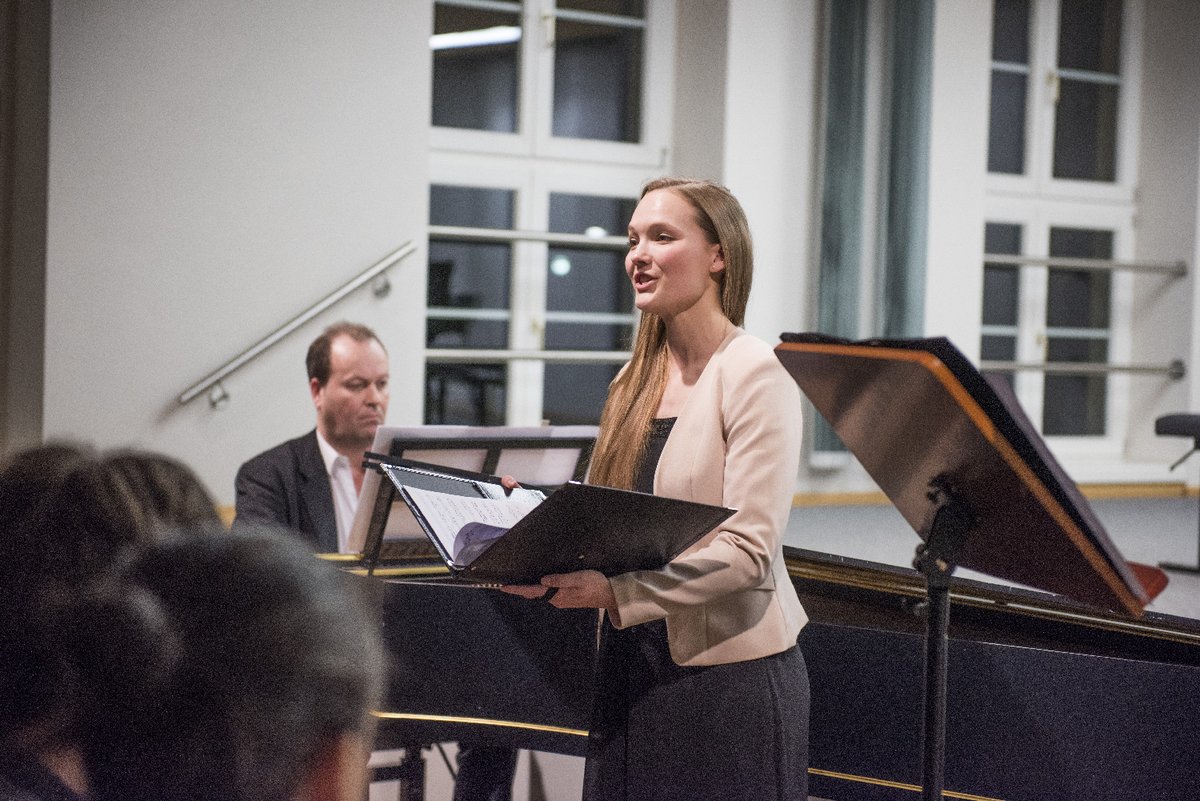 Eine Studentin steht singend auf der Bühne und wird von einem Dozenten am Klavier begleitet.