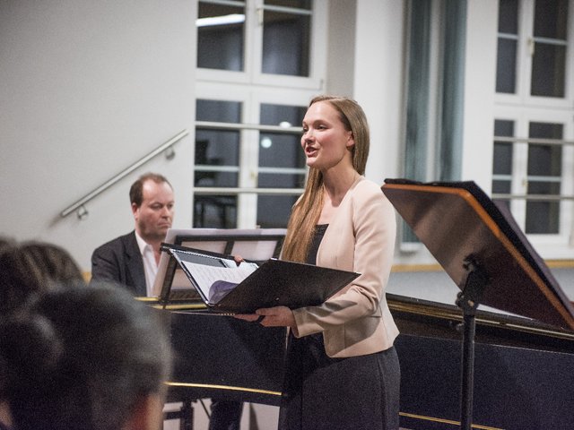 Eine Studentin steht singend auf der Bühne und wird von einem Dozenten am Klavier begleitet.