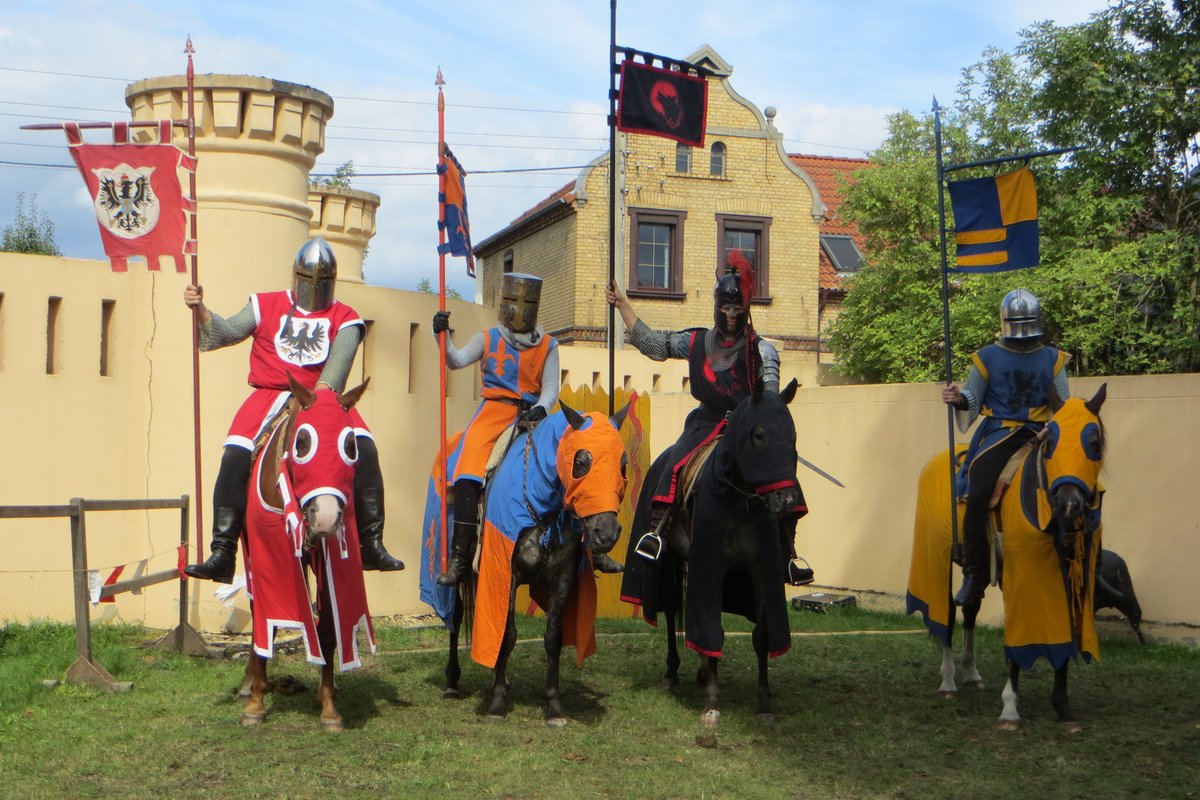 4 Reiter in mittelalterlicher Kleidung auf 4 Pferden. Im Hintergrund eine Burg