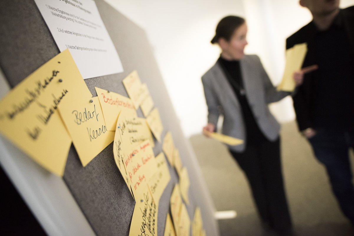 Pinwand mit Ideen, im Hintergrund Personen, die diskutieren 