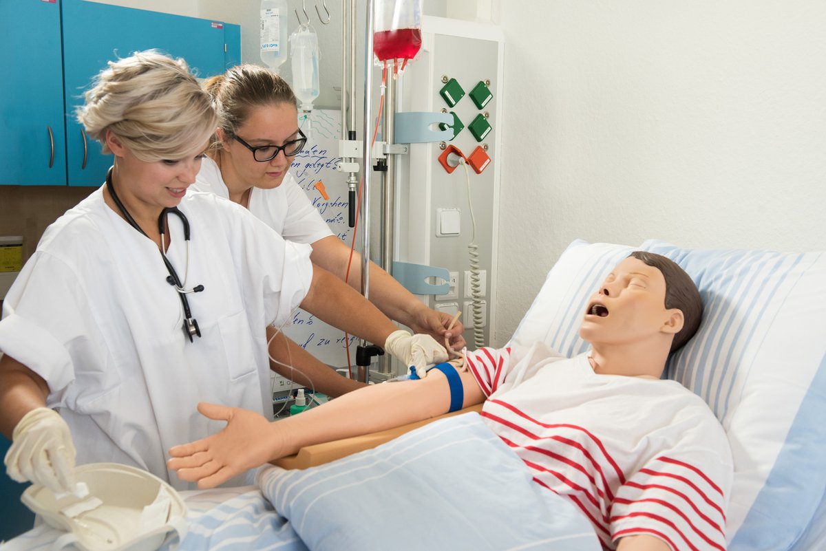 Zwei Studentinnen der Pflegewissenschaft am Bett einer Pflegepuppe.