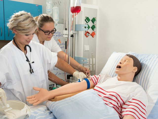 Two nursing students at the bedside of a nursing manikin.