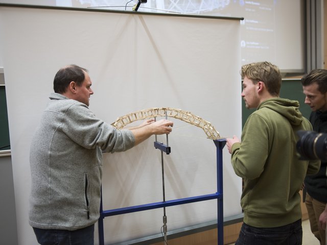 Zwei Studierende und ein Universitätsmitarbeiter befesetigen ein Brückenmodell auf dem Prüfstand.
