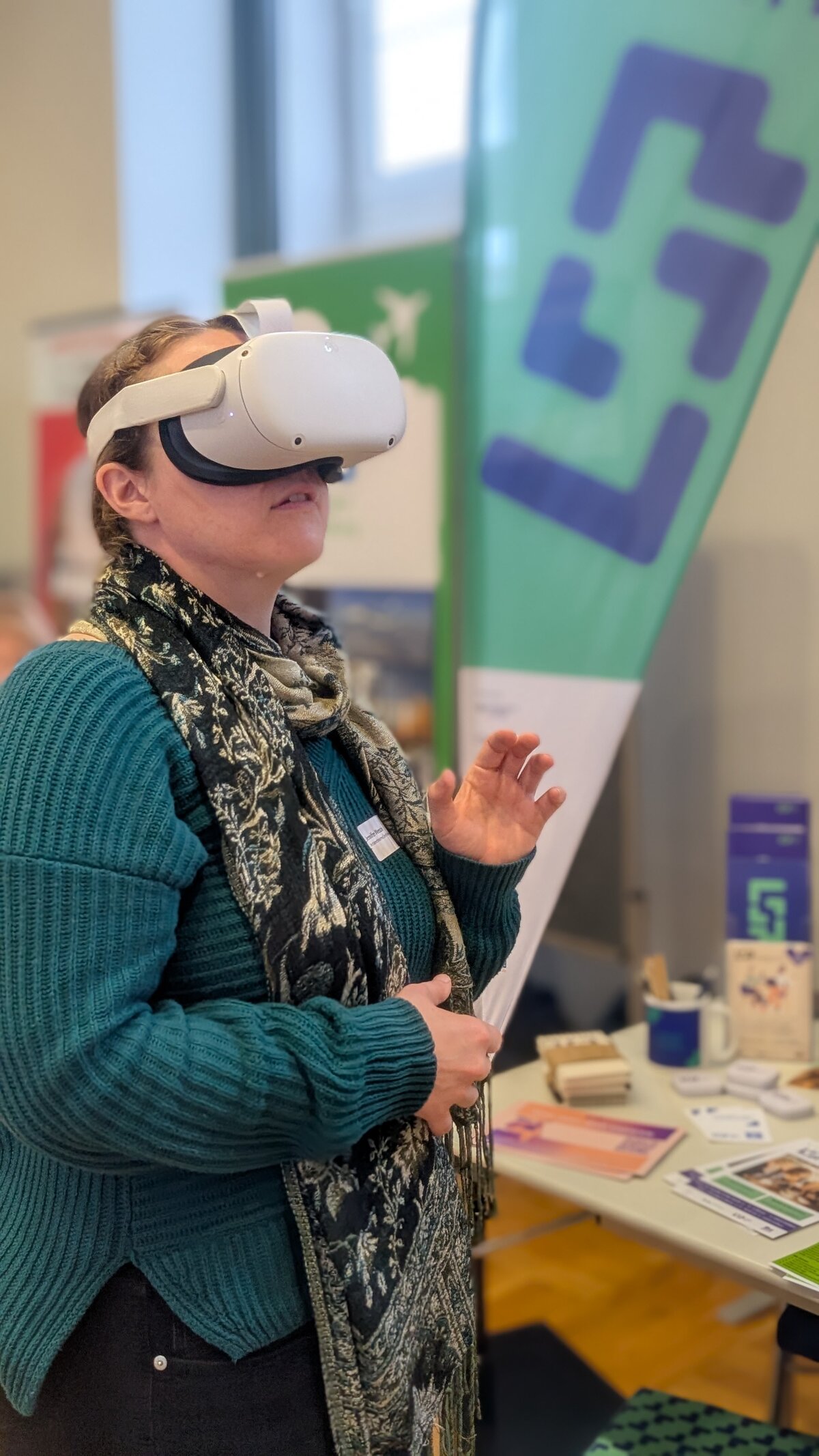 Eine Frau im grünen Oberteil hat eine VR-Brille auf und schaut leicht nach rechts oben.