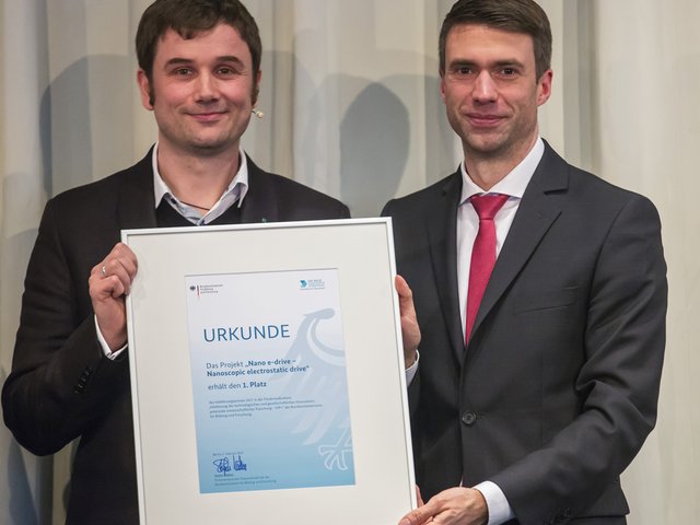 Preisträger Holger Conrad (links) und der Parlamentarische Staatssekretär Stefan Müller halten den Preis in den Händen