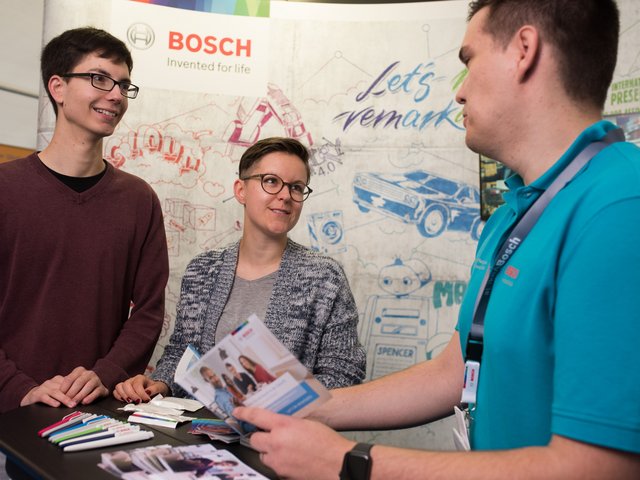 Besucher*innen und Aussteller der campus-X-change stehen im Gespräch am Messestand.