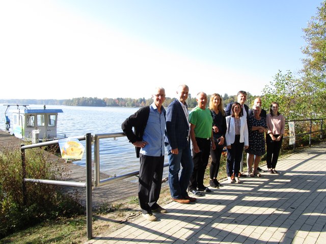 Gruppe steht vor dem See in Bad Saarow. Im Hintergrund ist der Forschungskatamaran zu sehen