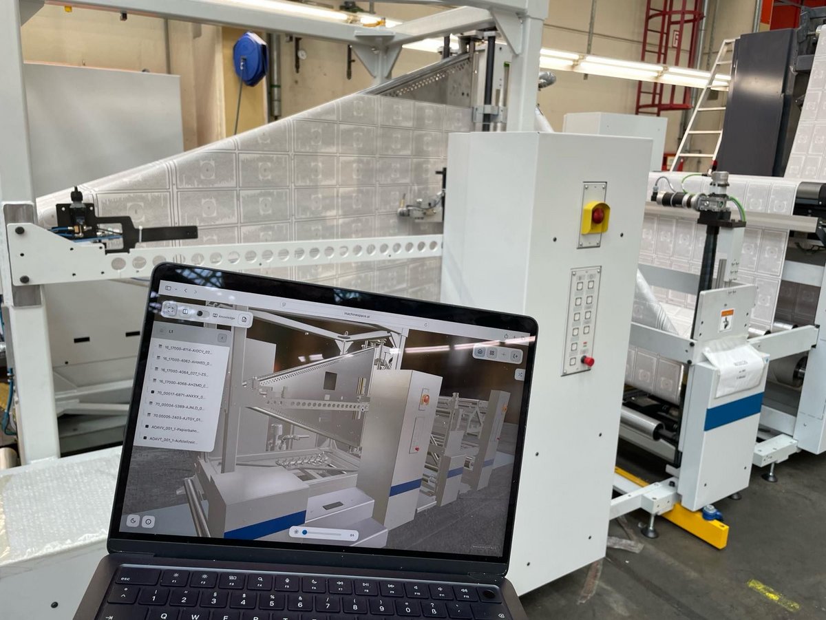 Konservierung von technischem Wissen am digitalen Zwilling einer Maschine für die Buchproduktion - im Vordergund Laptop mit der Mschine auf dem Monitor, die sich dahinter im Original befindet.