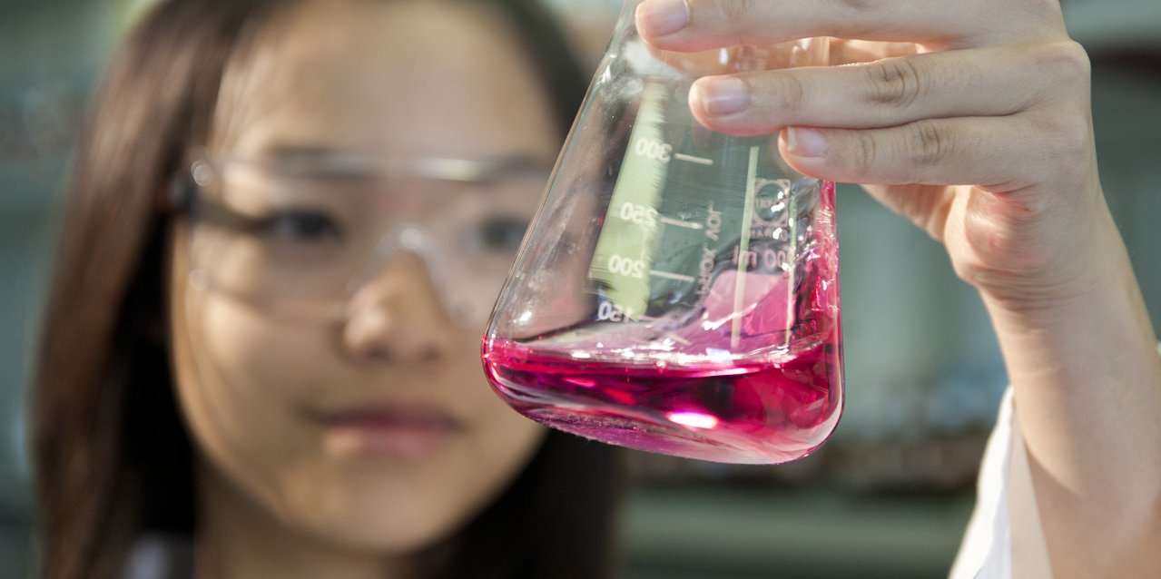 Studentin im Studiengang Materialchemie schwenkt Erlenmayerkolben mit pinker Flüssigkeit