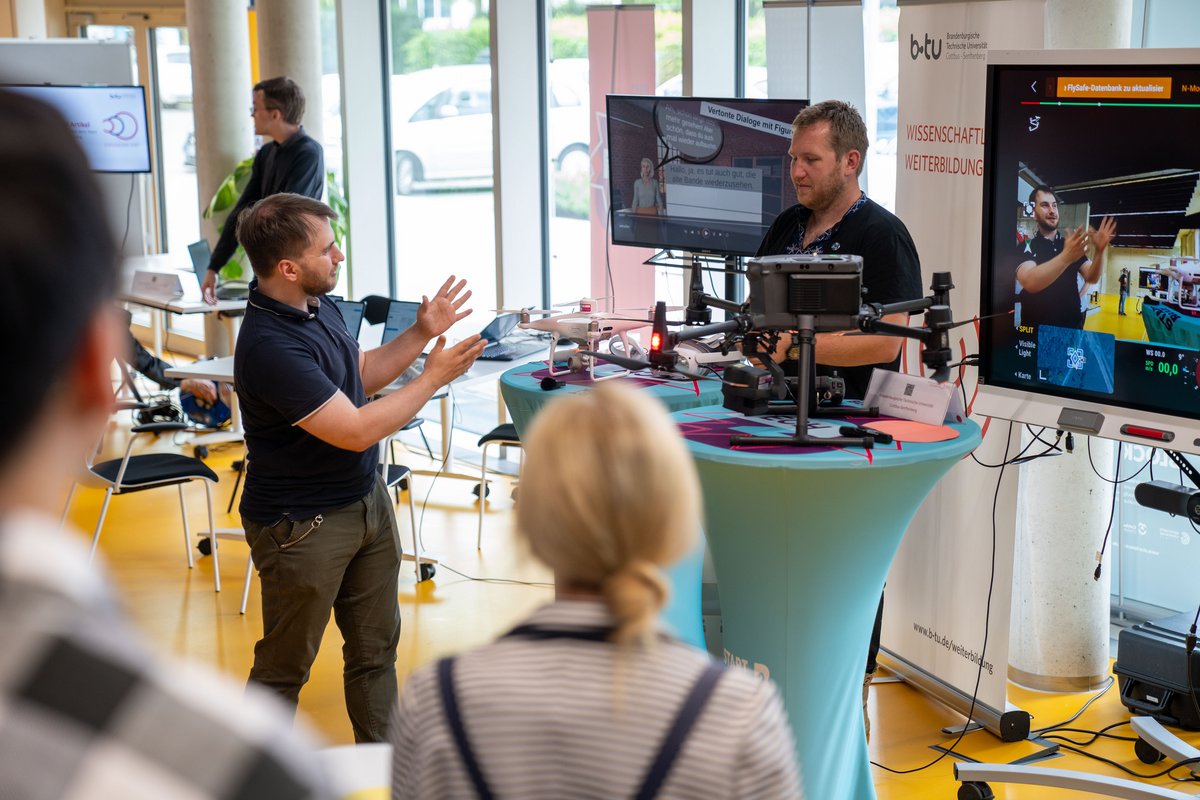 BTU-Mitarbeiter an einem Messestand geben Besuchern Erläterungen an einer Drohne zur zivielen Nutzung.  