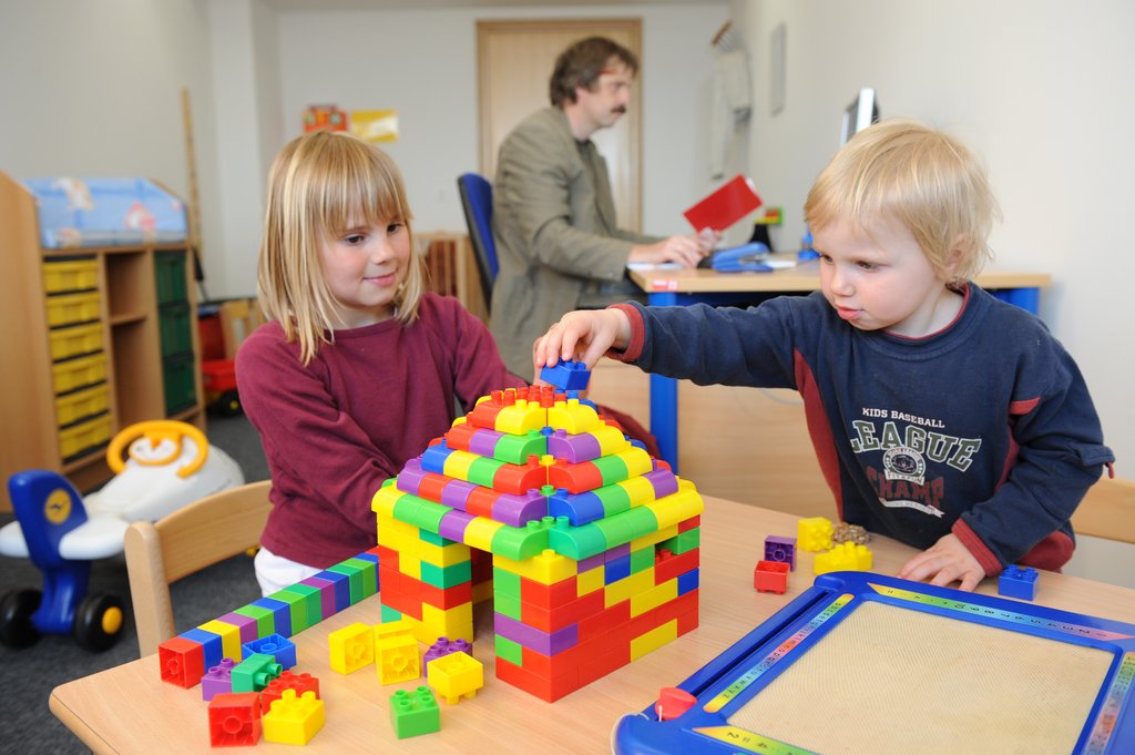Eltern-Kind-Zimmer Zwei Kinder spielen, im Hintergrund arbeitet ein Mann am PC