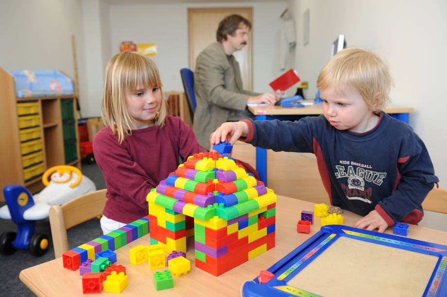 Eltern-Kind-Zimmer Zwei Kinder spielen, im Hintergrund arbeitet ein Mann am PC