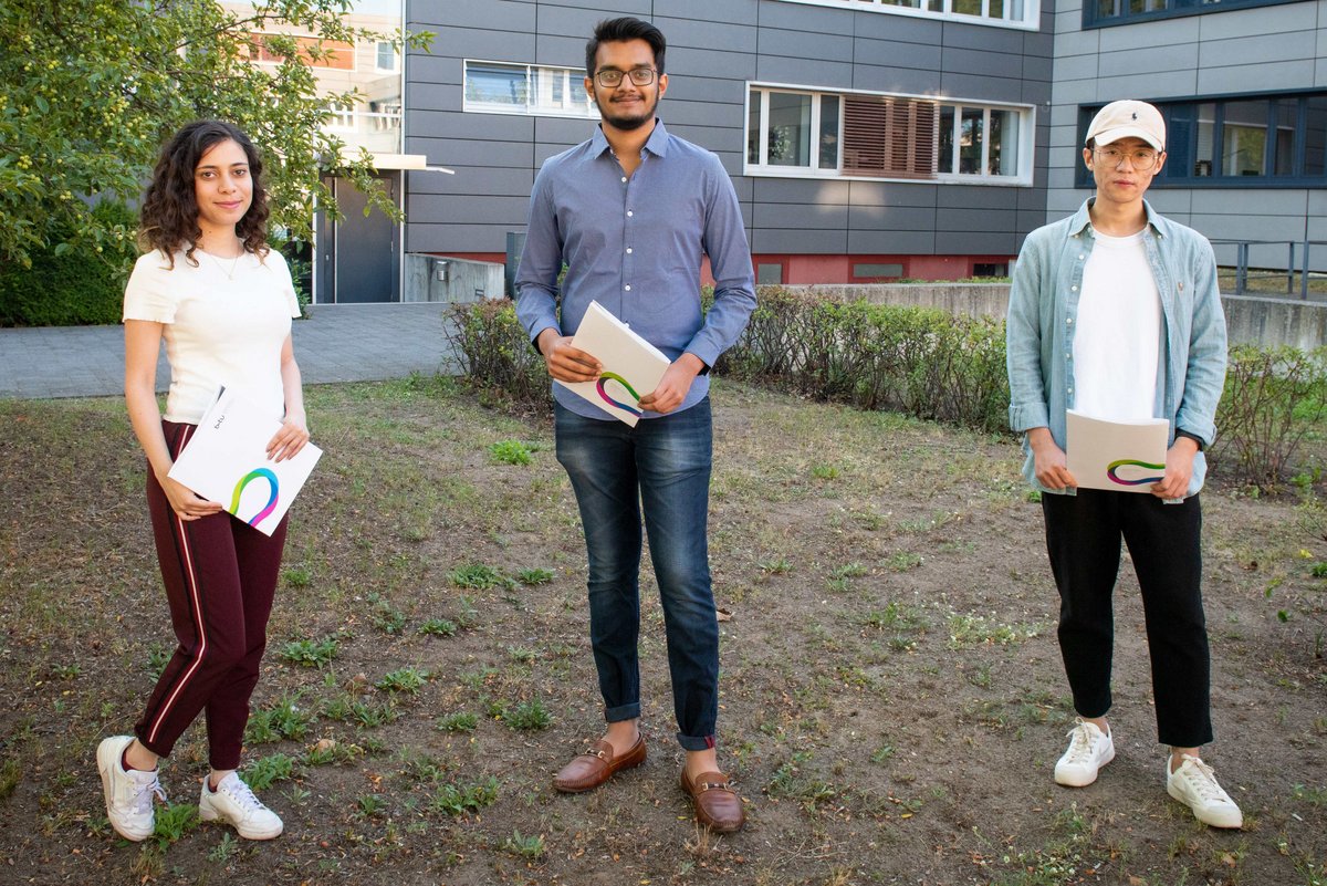 Die ESiSt-Absolvent*innen Roaa Mustafa, Sahil Dhavalbhai Nasit, Lanhao Luo (v. li.) stehen auf dem Campus und präsentieren ihre Zeugnisse. 