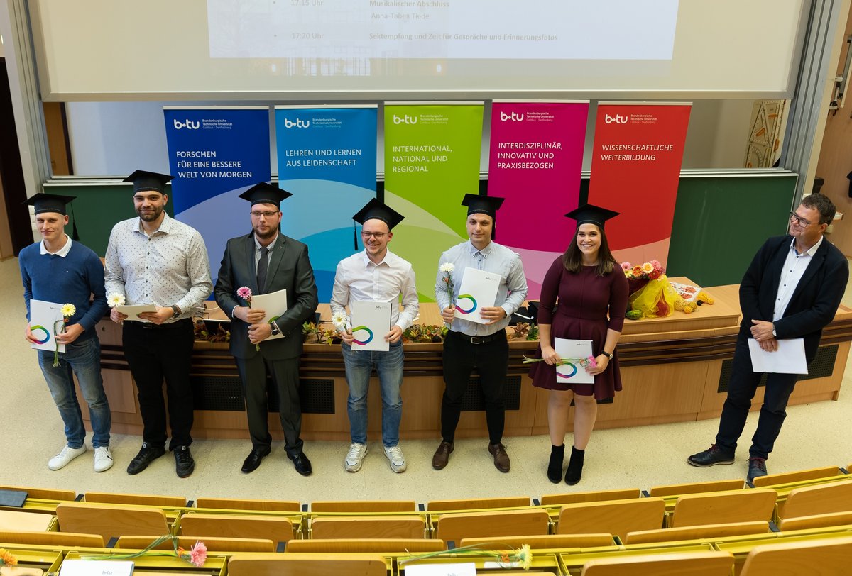 Graduates stand in the lecture hall with their certificates.