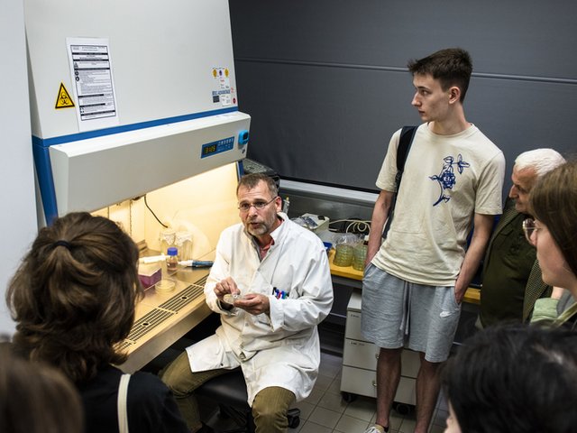 A group of pupils stand in a laboratory surrounding a professor in a lab coat.