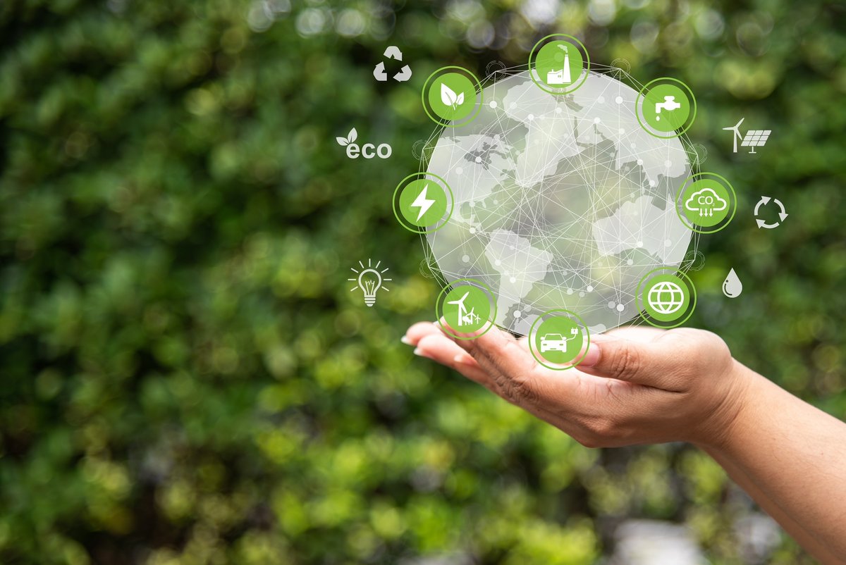 Sinnbild Eco-Kreislaufwirtschaft: symbolische Icons in einer transparenten Kugel auf einer Handfläche, grüner Hintergrund mit Blattwerk