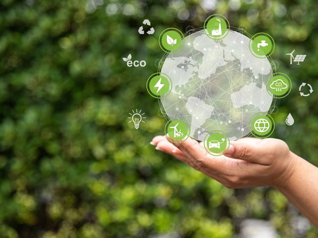 Sinnbild Eco-Kreislaufwirtschaft: symbolische Icons in einer transparenten Kugel auf einer Handfläche, grüner Hintergrund mit Blattwerk