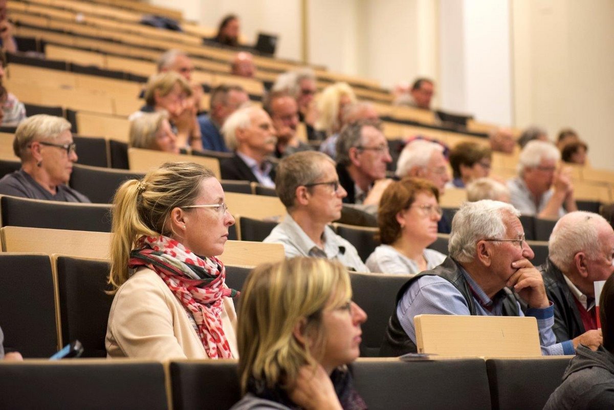 Younger and older people sit in the lecture hall and follow a lecture.