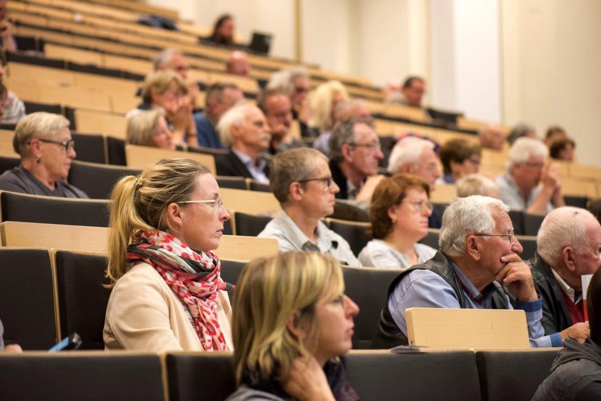 Jüngere und ätere Personen sitzen im Hörsaal und folgen einer Vorlesung.