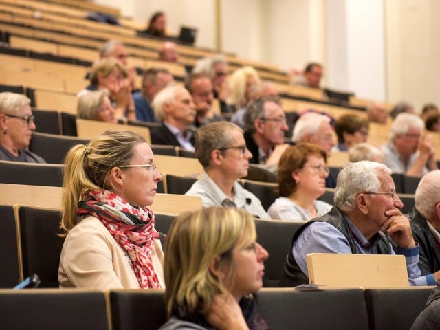 Younger and older people sit in the lecture hall and follow a lecture.
