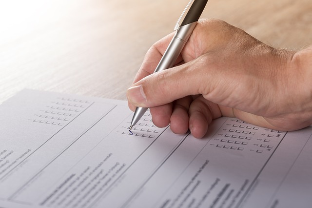 Hand hält Stift und ergänzt Text auf Blatt Papier