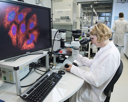 A person in a white lab coat is sitting at a microscope, examining something.