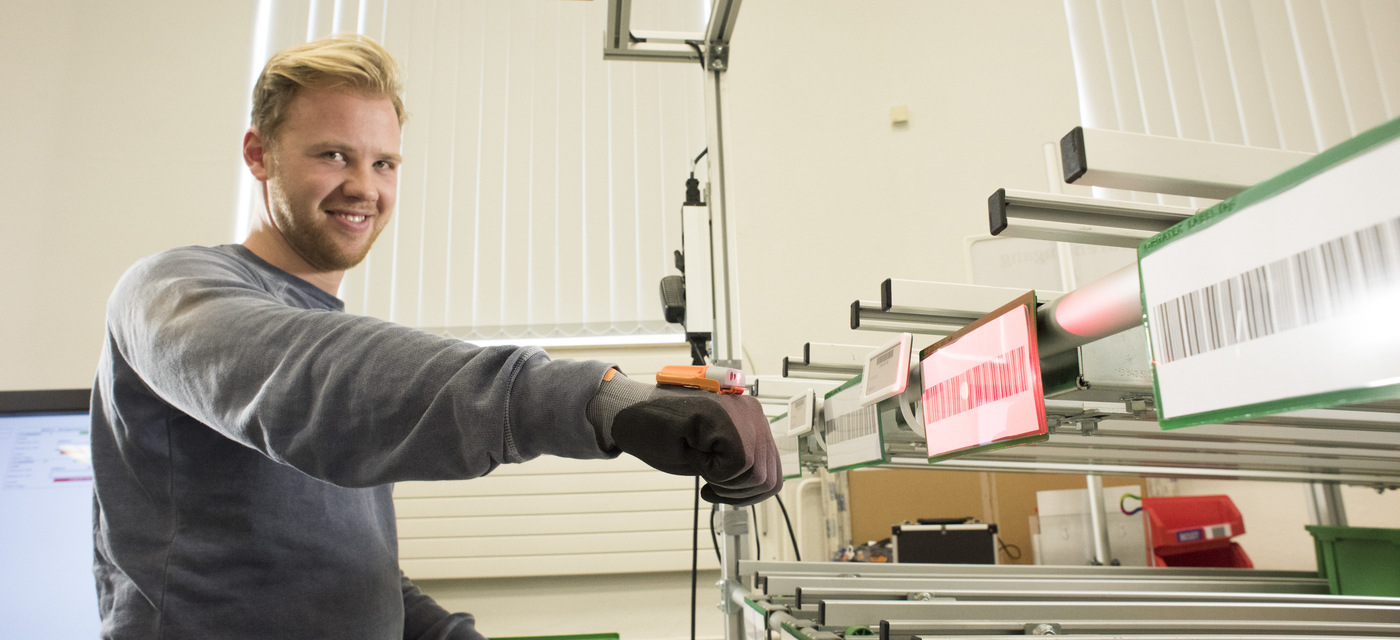 Student in the bachelor study programme business administration and engineering scans labels with a scan glove in the model factory