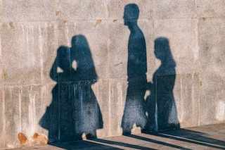 Shadow of four people walking in the same direction against exterior wall of a house