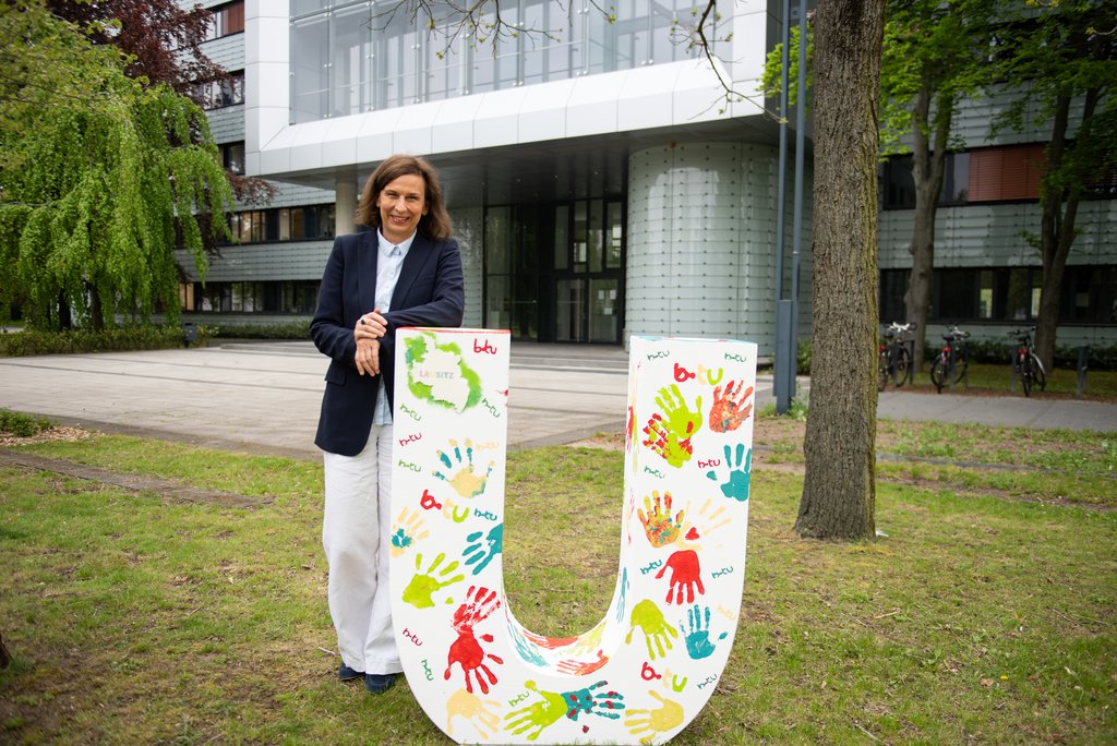 Präsidentin Prof. Gesine Grande mit dem großen "U" vor dem Hauptgebäude der Universität. Der Buchstabe wurde für die Präsentation von "VIELFALT LAUSITZ" am 18. Mai 2021 auf dem Cottbuser Altmarkt von BTU-Angehörigen gestaltet. (Foto: BTU, Spencer Vane)