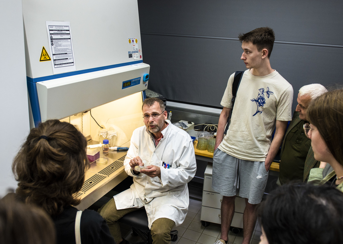 A group of pupils stand in a laboratory surrounding a professor in a lab coat.