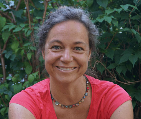 woman , smiling, in front of a greent hedge