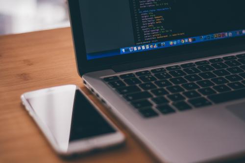 Aufgeklappter Laptop, daneben ein Handy auf einem Tisch