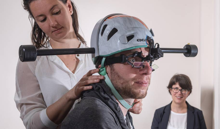 Dr. Cecilia Ramaioli (links) überprüft den Sitz des Helms mit Gewichten bei einem Probanden. Prof. Nadine Lehnen stellt im Hintergrund den Computer für das Experiment ein