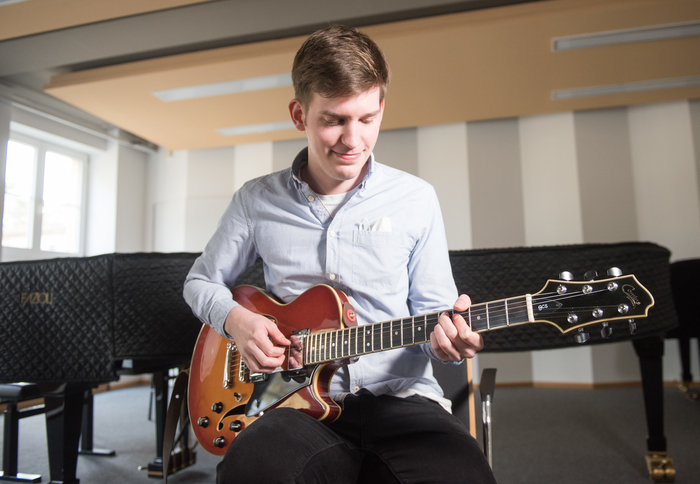 Student mit Gitarre im Konzertsaal