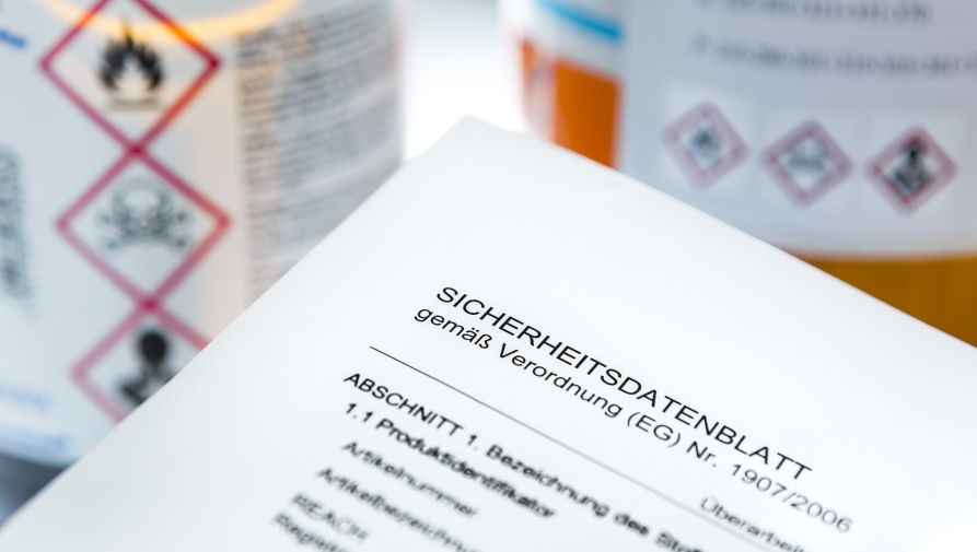 ein Sicherheitsdatenblatt vor Flaschen mit Gefahrstoffen